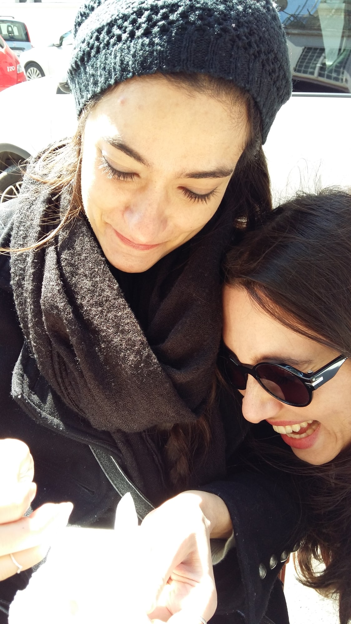 Daniela and Paola lean together outdoors, one wearing a knitted hat.