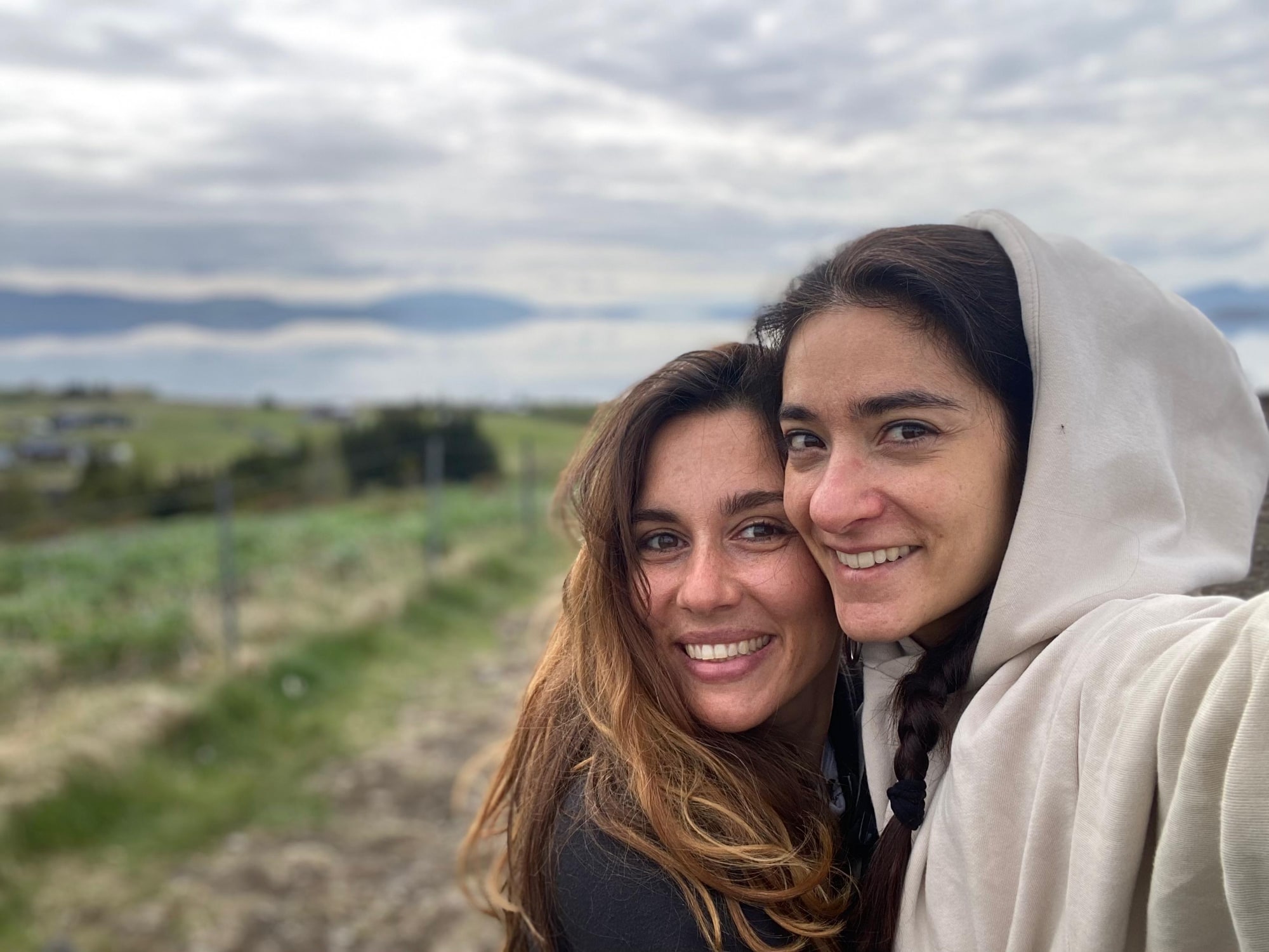 Daniela and Paola smile together outdoors beside a field.