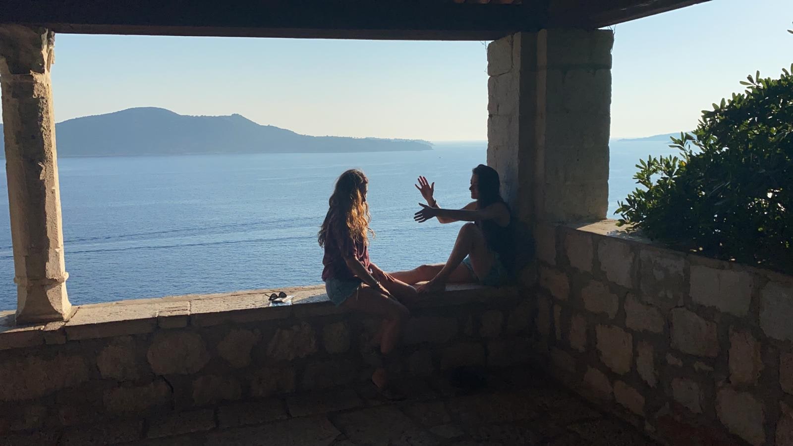 Friends sit in a shaded terrace overlooking the sea.
