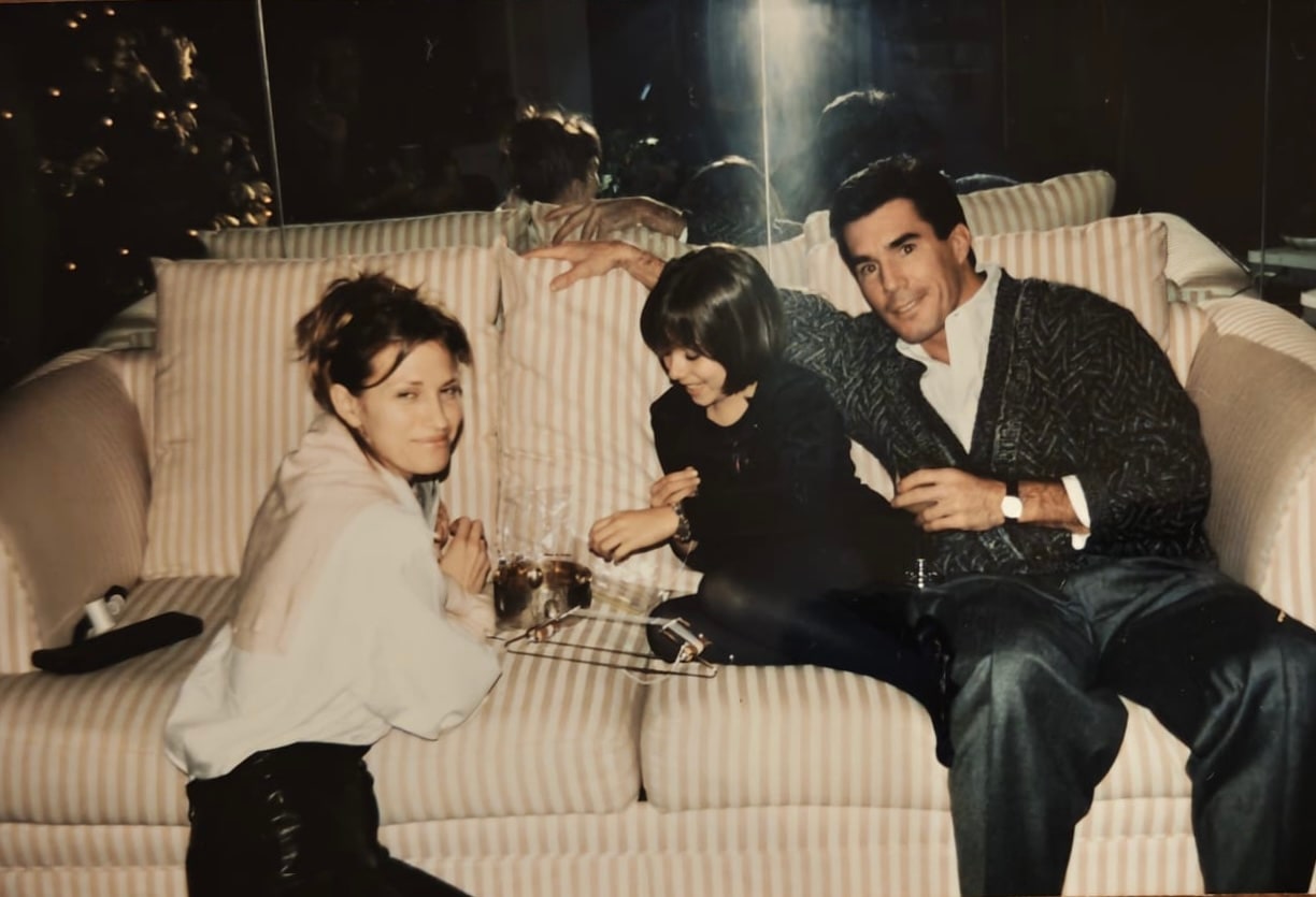 Daniela sits with friends of her parents on a striped sofa.