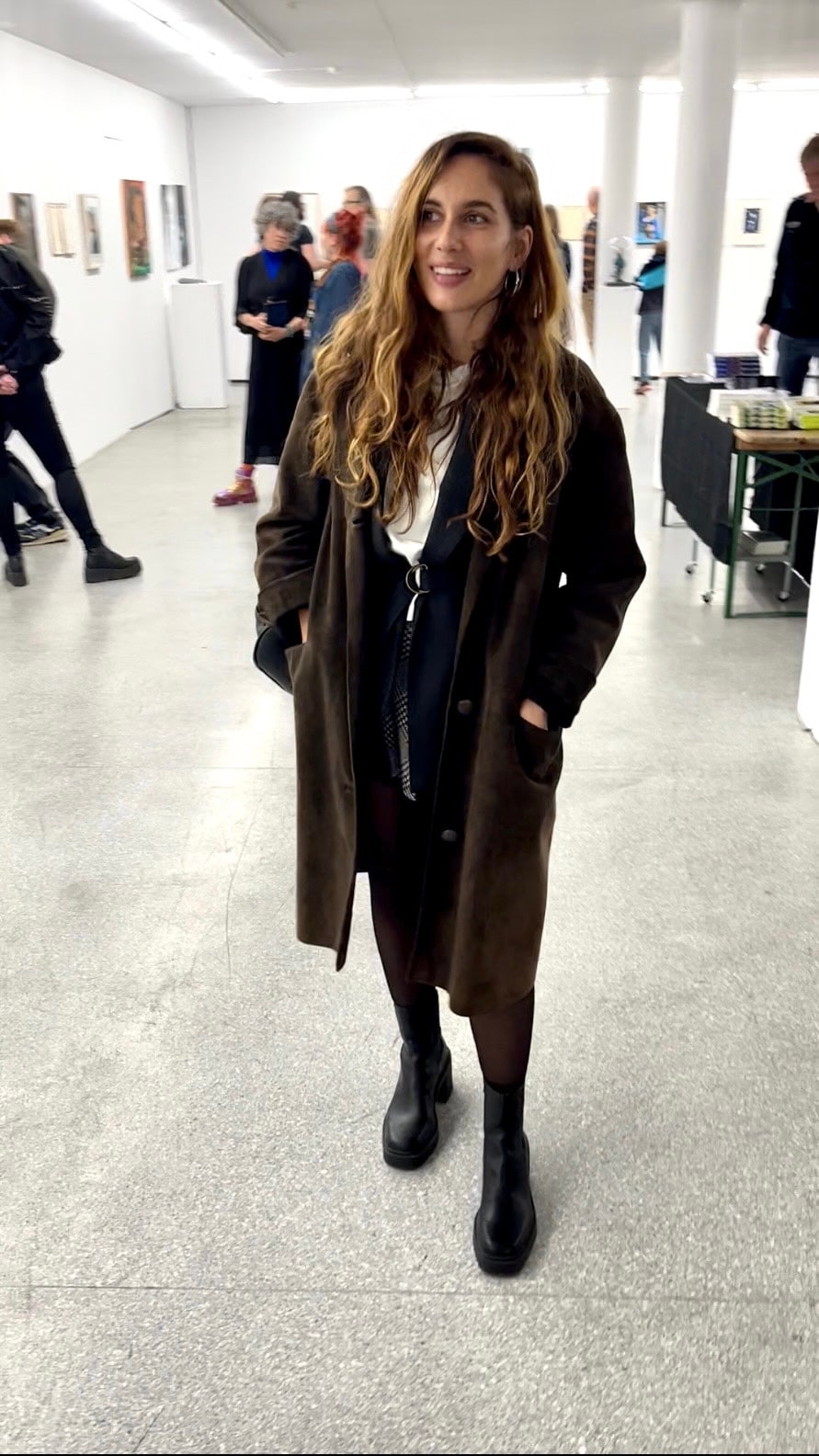 Daniela stands in a gallery with paintings and visitors behind her.