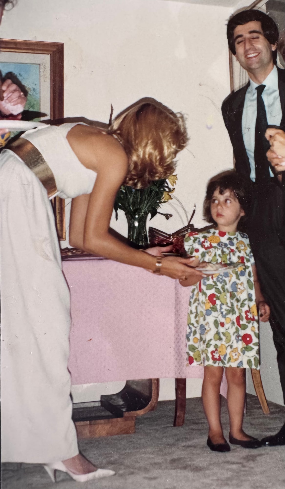 Daniela, in a floral dress, stands with her father and a woman.