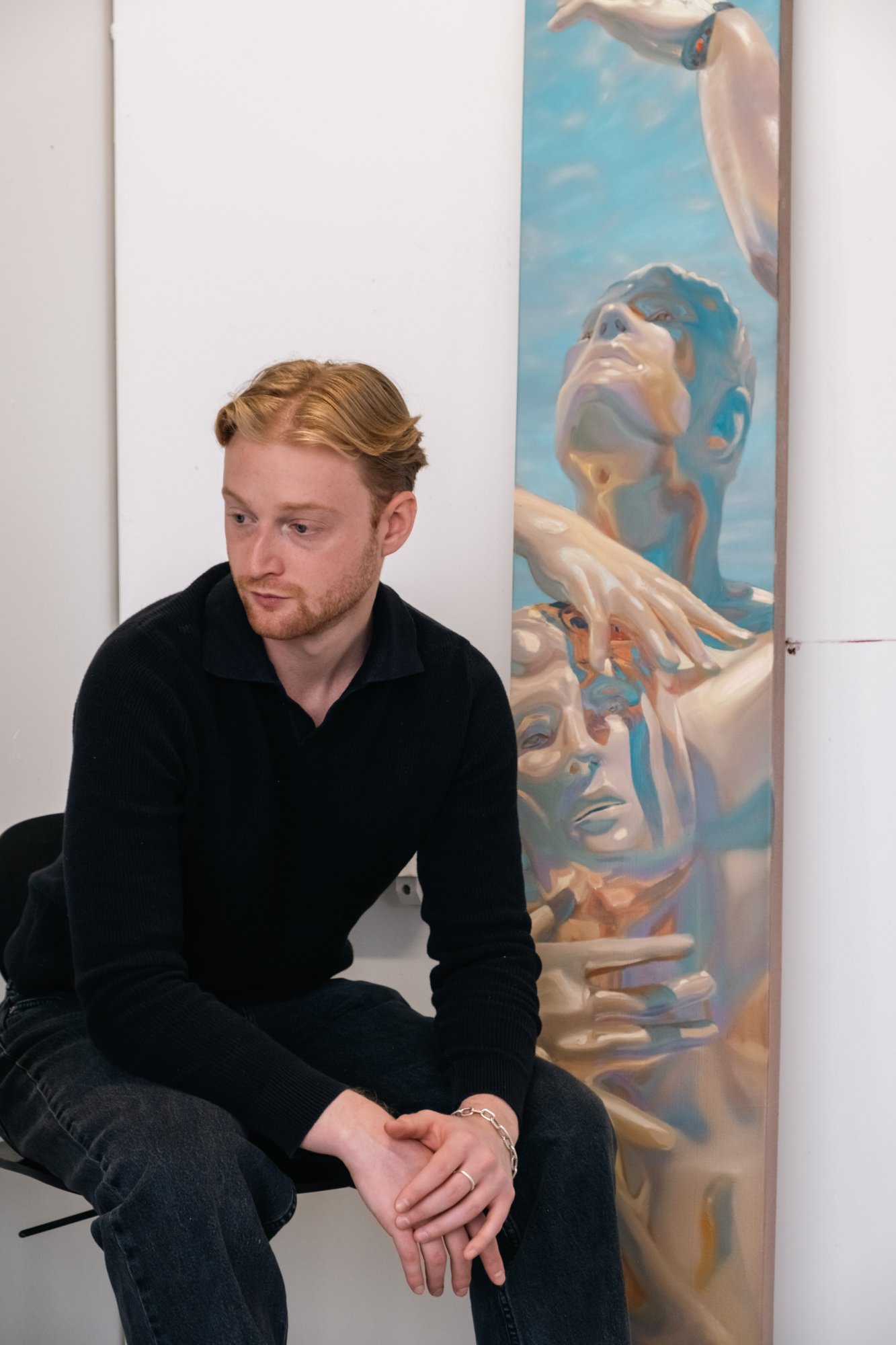 Ethan Platt sits beside a tall painting of intertwined reflective figures