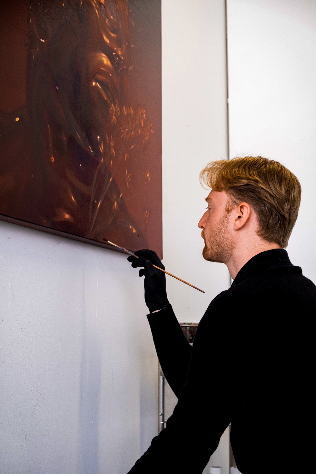 Ethan Platt applies paint to a large portrait with a long-handled brush