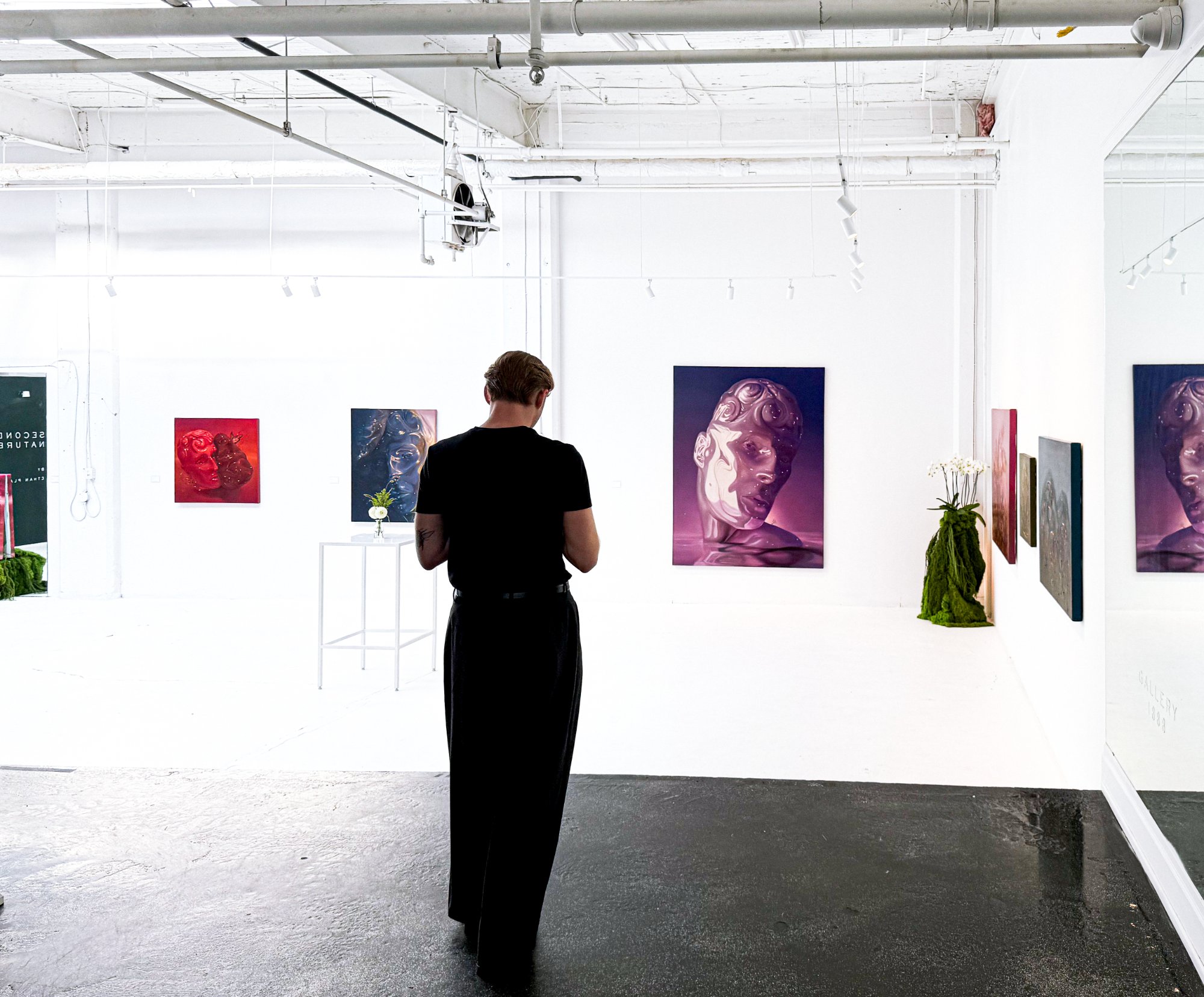 Ethan Platt stands in a gallery facing his paintings