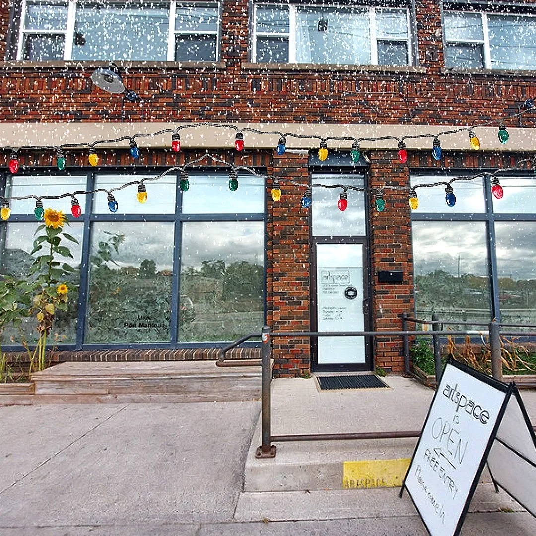 Artspace’s brick storefront with tall windows and an Open sign on the sidewalk. Coloured string lights and falling snow are added over the photo.
