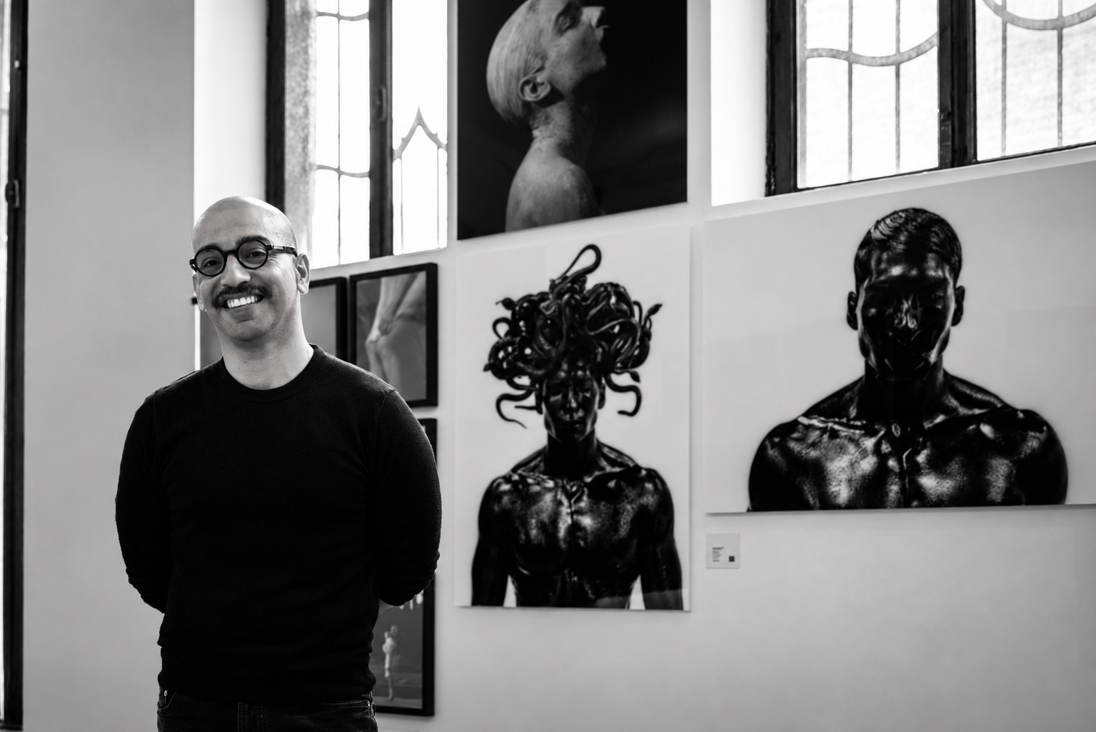 Rafael Montalvo smiles in a gallery beside large black-and-white prints, including a male Medusa crowned with snakes.